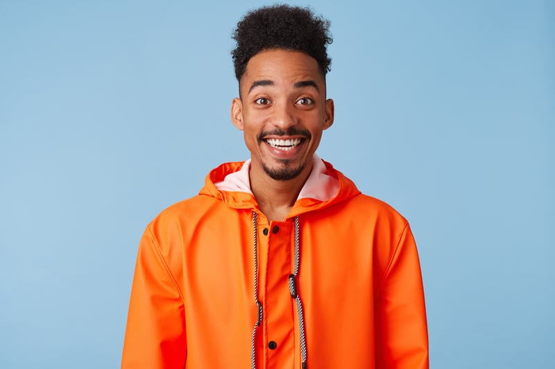 Man in orange jacket standing in front of light blue background