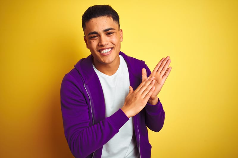 Man in white shirt and purple zip-up jacket standing in front of yellow background