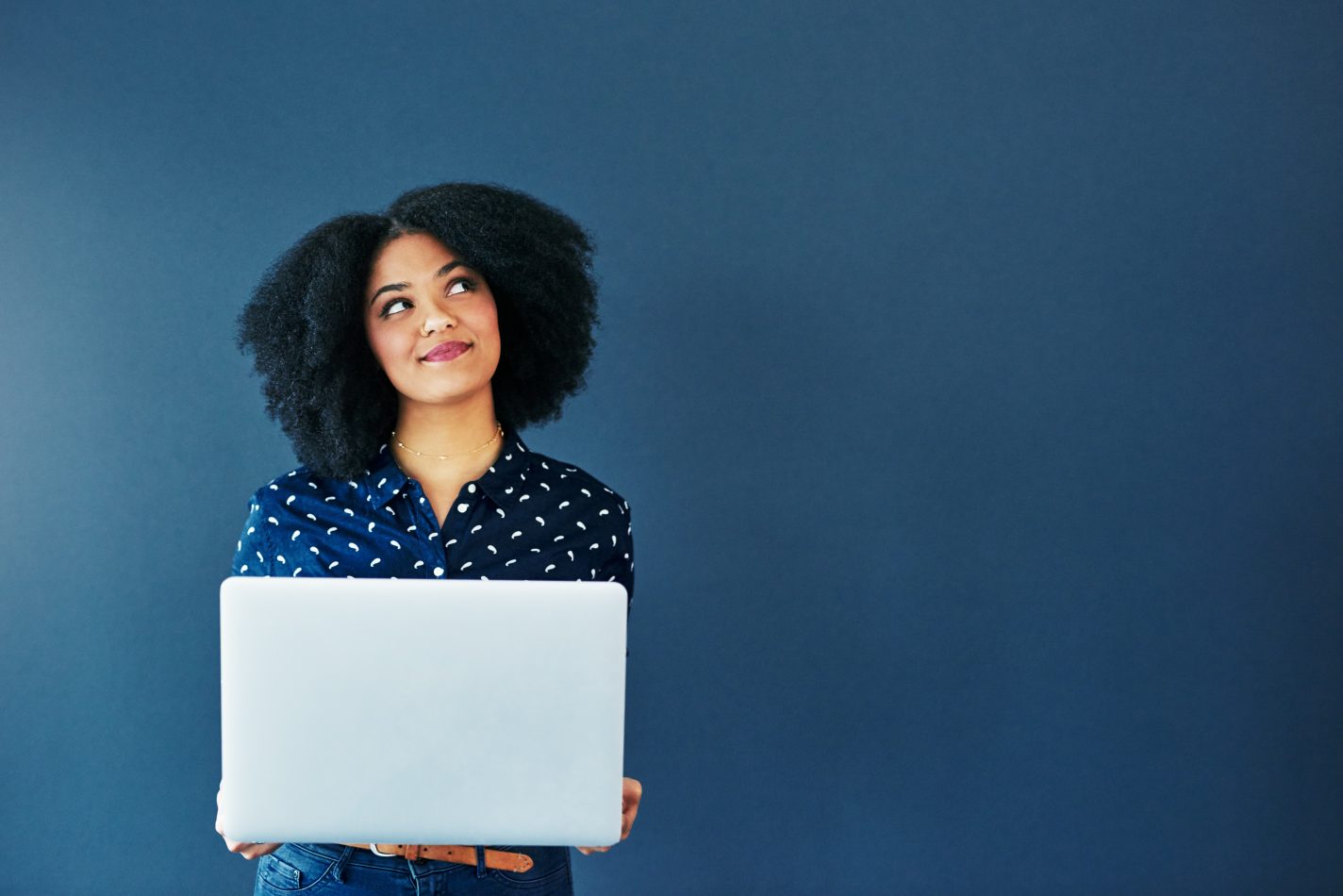 smiling woman holding laptop, looking up in thought