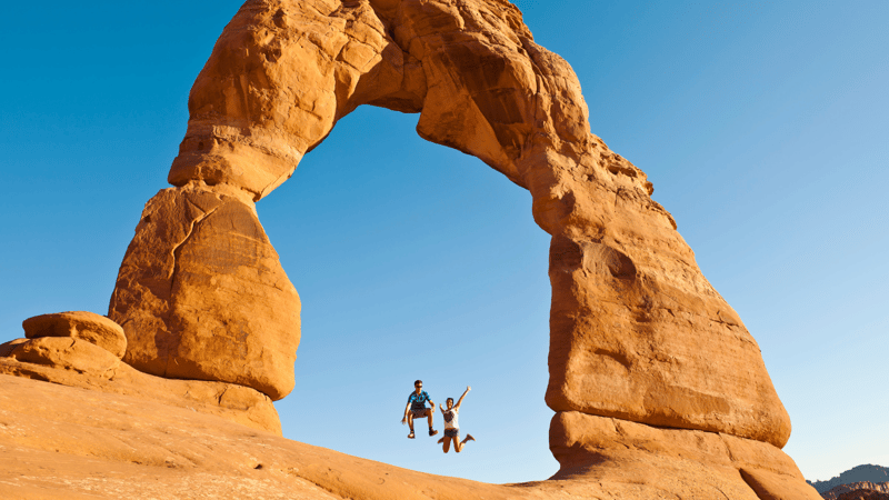 Couple jumping under rock arch